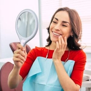 A woman gazes into a mirror, smiling brightly, reflecting happiness and self-acceptance.