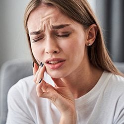 Woman in need of an emergency dentist holding face because of Jaw Pain