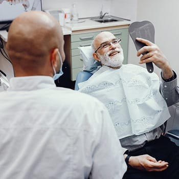 Man sitting in dental chair looking at new implants in a mirror