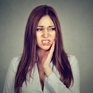 A young woman clutching her jaw in pain, in need of root canal treatment with Shwarts Family Dentistry.