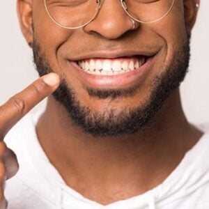 A young man pointing to his straight, white teeth.