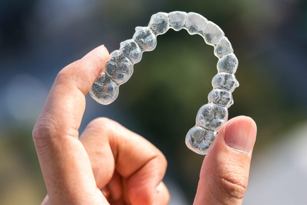 An Invisalign tray being held up between two fingers.