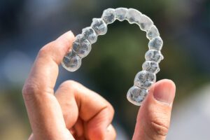 An Invisalign tray being held up between two fingers.